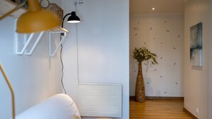 Un intérieur moderne avec un radiateur blanc, un tabouret rond en bois, une plante en pot et une lampe fixée au mur.