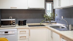 Une cuisine moderne avec des meubles blancs, un évier en acier inoxydable, un four à micro-ondes, un grille-pain et une plante.