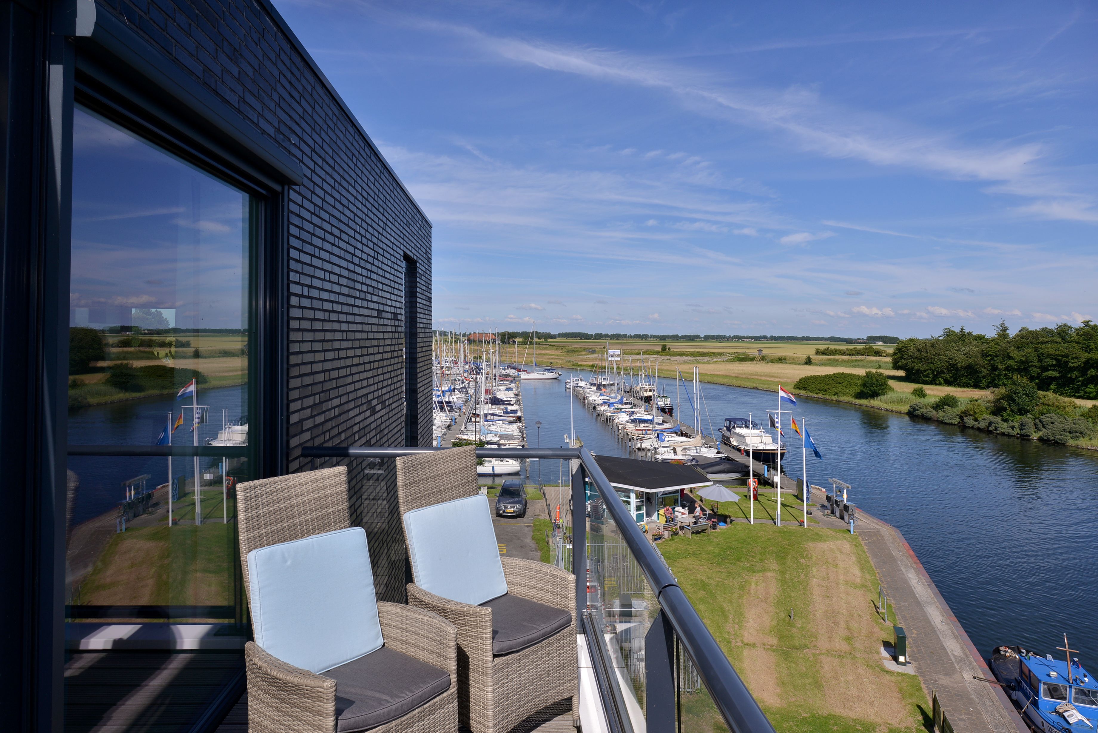 A balcony with wicker chairs, a view of a marina with boats, and a river.