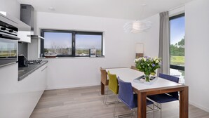 Une cuisine moderne dotée d’une grande fenêtre, un coin repas avec une table et des chaises, et une vue sur la campagne.