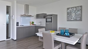 Une cuisine moderne avec des meubles gris, un plan de travail blanc et un coin repas avec une table dressée pour deux personnes.