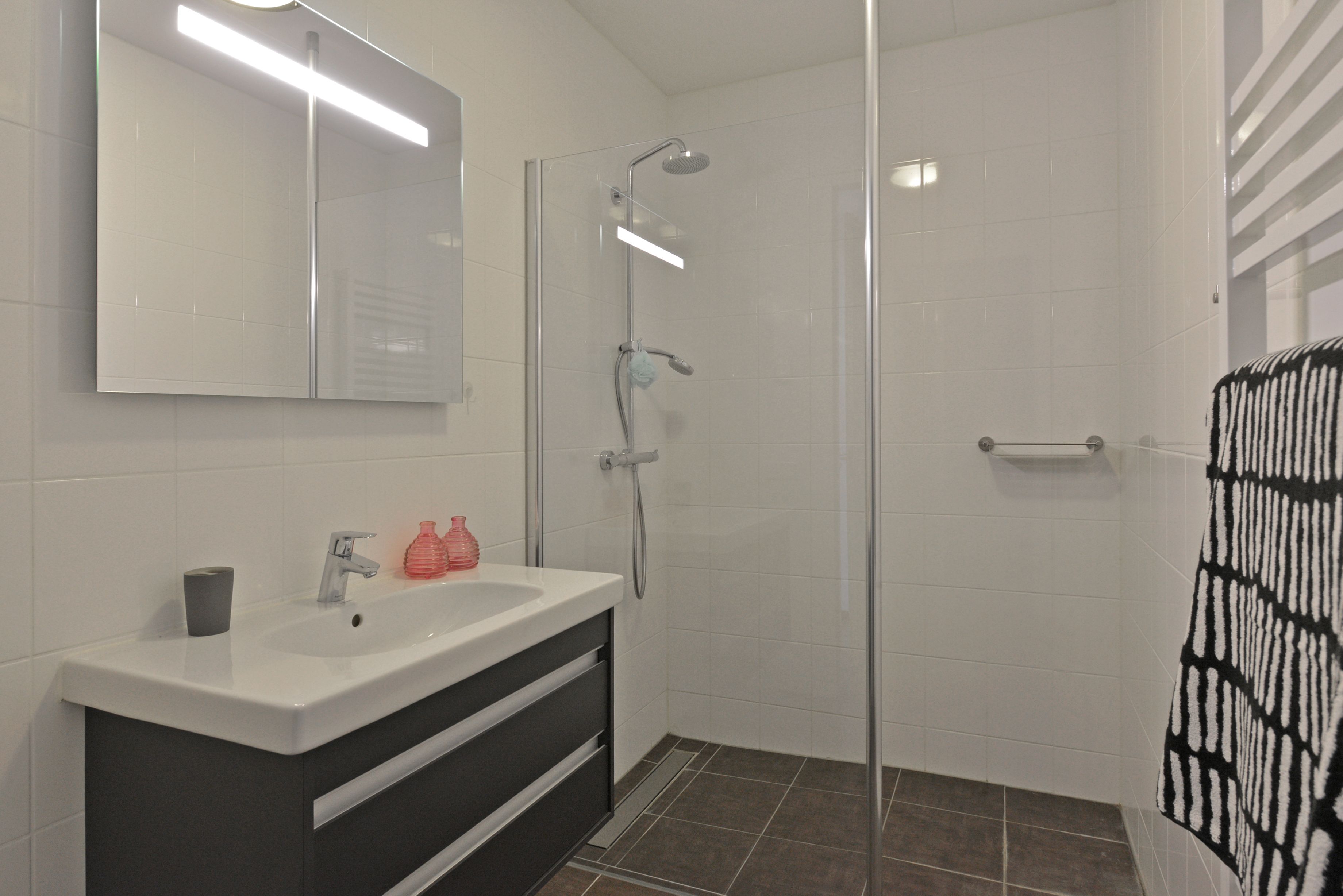 A modern bathroom with a white sink, a mirror, a shower, and a towel rack.