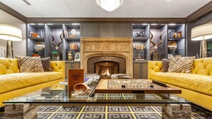 Een moderne woonkamer met een open haard, twee gele banken, een salontafel en decoratieve wandplanken met boeken en gewei.