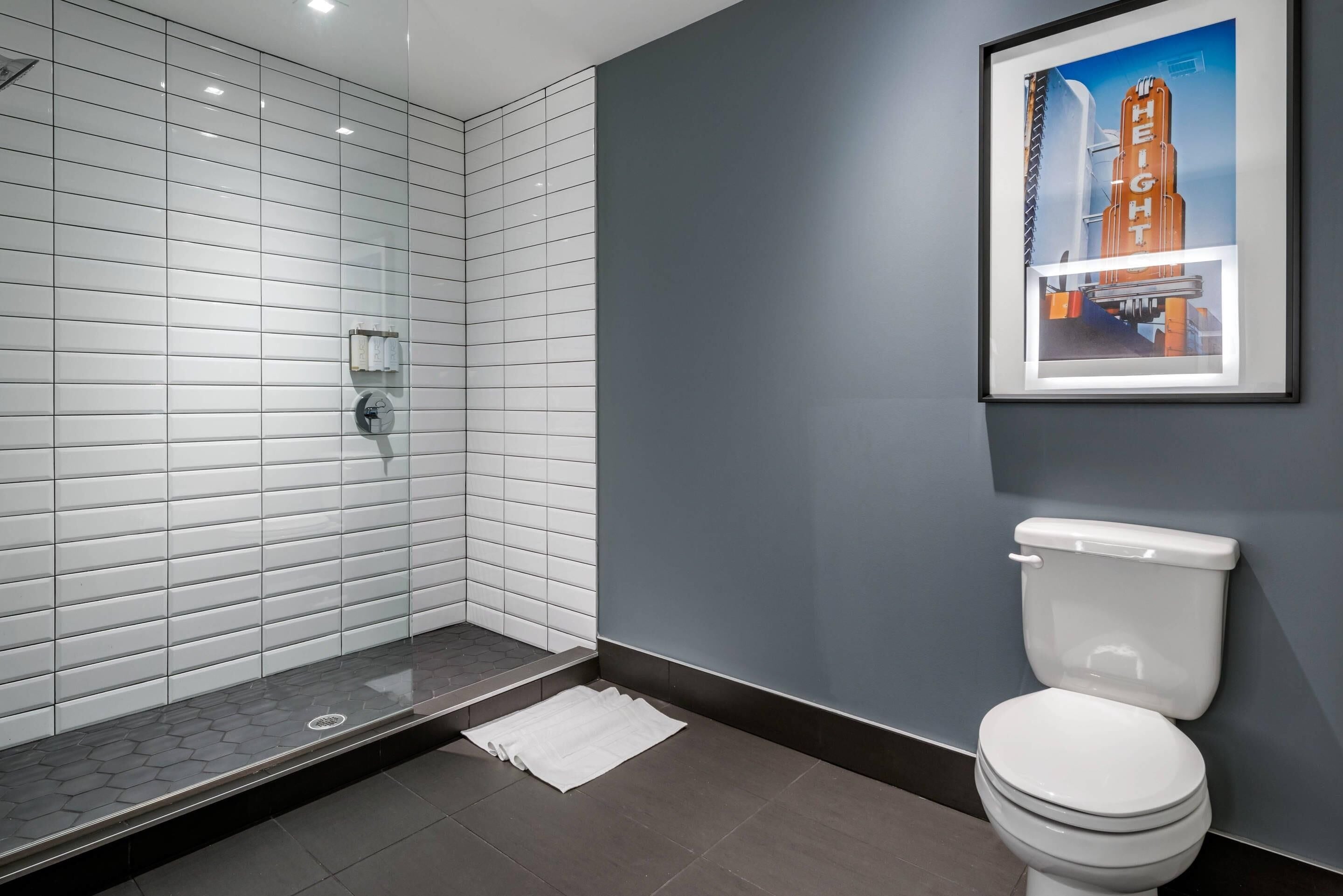 Un baño moderno con inodoro blanco, cabina de ducha con vidrio y un cuadro de un edificio en la pared.