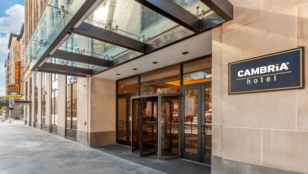 Een hotelentree met een glazen gevel, een draaideur en een bord waarop staat Cambria Hotel.