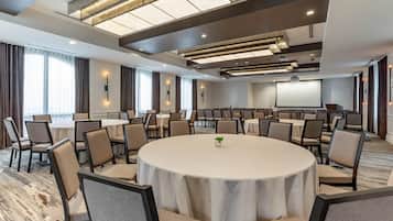 Un salón de conferencias con mesas redondas, sillas y una pantalla para proyector.