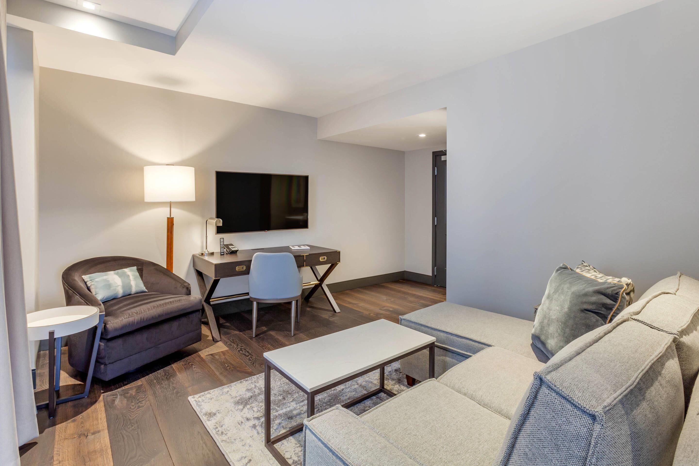 A modern living room with a sofa, armchair, desk, and TV.