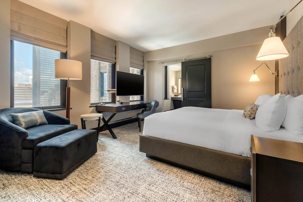 Ein modernes Hotelzimmer mit einem großen Bett, einer Couch, einem Schreibtisch und einem Flachbildfernseher, mit Blick auf die Stadt.