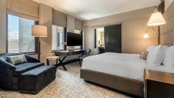 Habitación de hotel moderna con una cama grande, un sofá, un escritorio y un televisor de pantalla plana, y vista a la ciudad.