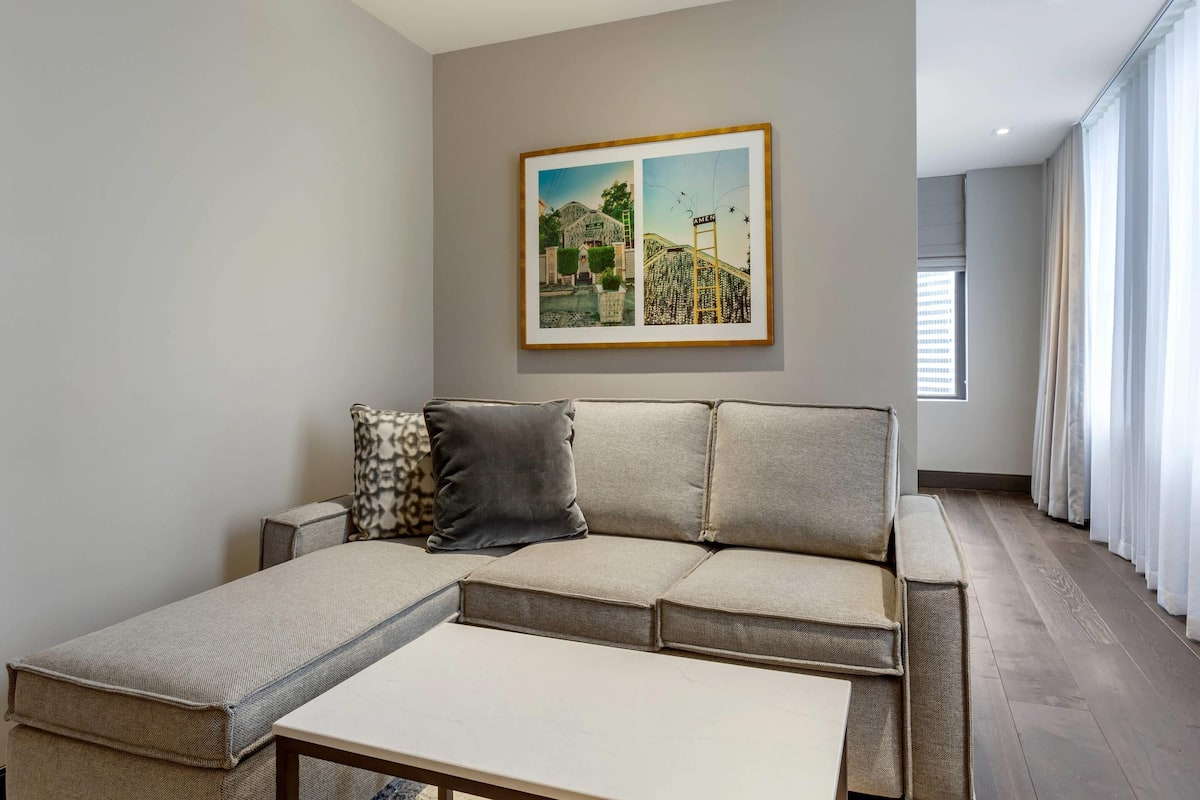 Ein modernes Wohnzimmer mit einem Ecksofa, einem kleinen Tisch und einem gerahmten Bild an der Wand.