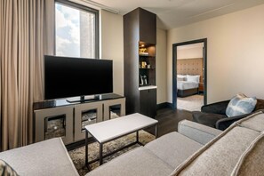 A modern hotel room with a flat-screen TV, a sofa, a coffee table, a bookshelf, and a bed.