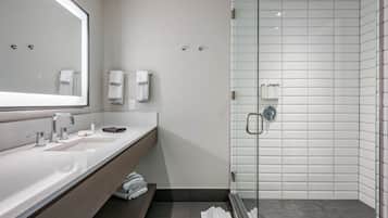 A modern bathroom with a large mirror, two sinks, a glass shower enclosure, and a towel rack.