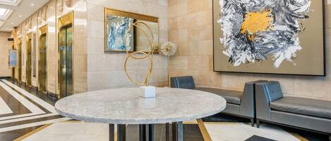 A lobby with a marble floor, a round table, a sofa, and a large abstract painting.