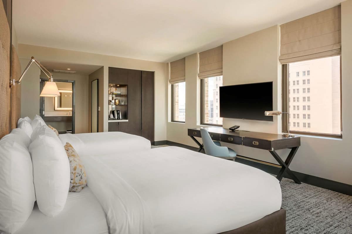 Ein Hotelzimmer mit einem großen Bett, einem Schreibtisch mit Fernseher und einem Fenster mit Blick auf Gebäude.