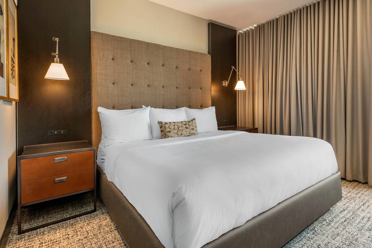 Ein Hotelzimmer mit einem großen Bett, einem hölzernen Kopfteil, einem Nachttisch mit Schubladen und zwei Wandleuchten.