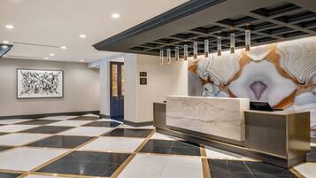 A hotel reception area with a marble reception desk, a large abstract painting on the wall, and a patterned floor.
