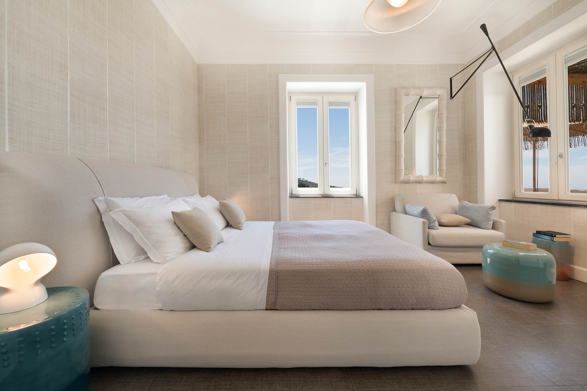 A modern bedroom with a large bed, a sitting area with a chair and ottoman, and a window with a view.