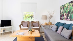 A living room with a sofa, two wicker chairs, a coffee table, a TV, a lamp, and a cactus wall art.