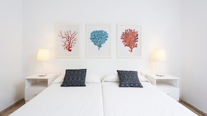 A hotel room with two beds, white walls, and three framed artworks depicting coral-like structures.