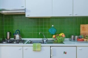 A kitchen with green tiles, a kettle, a sink, and a fruit basket.