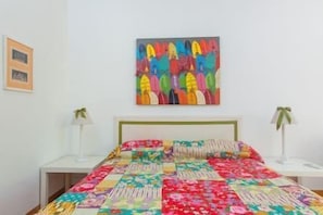 A bed with a colorful quilt, a white wall, and a framed picture.