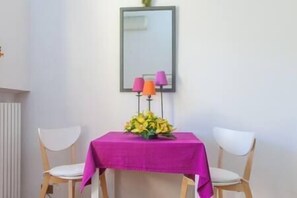 Ein Essbereich mit einem Tisch, der mit einer leuchtend rosa Tischdecke bedeckt ist, zwei weißen Stühlen und einem Spiegel an der Wand.