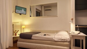 A hotel room with a bed, a bedside table with a lamp, a mirror, and a TV displaying a cityscape. - Sunny apartment view on St. Peter's secure parking (Roma)