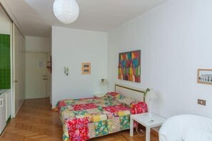 Ein Schlafzimmer mit einem Bett, einem Nachttisch, einer Lampe, einem Gemälde und einer Tür.