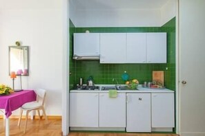 Eine kleine Küche mit weißen Schränken, einer grünen Spritzschutzleiste und einem Essbereich mit Tisch und Stuhl.