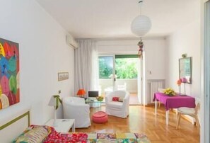 Ein helles Zimmer mit einem Bett, einem Schreibtisch, einem Stuhl und einem Tisch mit lila Tischdecke.
