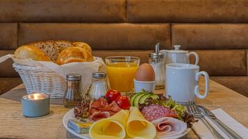 A breakfast setting with bread, eggs, cheese, ham, tomatoes, and a drink on a table.