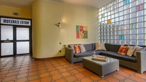 Eine Lobby mit einer Couch und einem Couchtisch, eine Tür mit der Aufschrift 'HOTEL CARRINGTON' und ein großes Fenster mit bunten Glasscheiben.