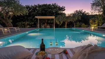 Una piscina con lettini e una zona relax coperta, immersa nel verde.