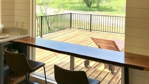 A balcony with a wooden deck, a black metal railing, and a view of a green landscape with trees.
