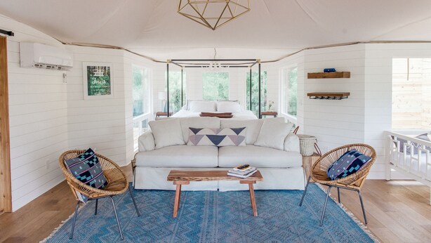 A cozy room with a white sofa, two wicker chairs, a wooden coffee table, and a geometric ceiling light.