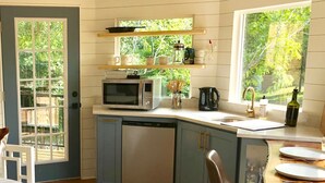 A compact kitchen with a microwave, coffee maker, and a sink. There is a dining area with a table and chairs.