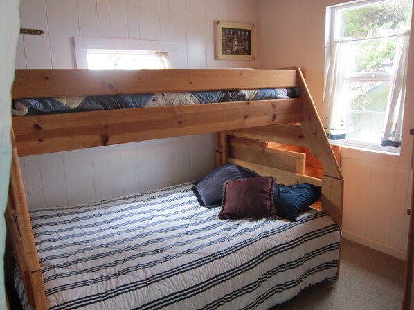 Una cama litera con una colcha a rayas, una ventana pequeña que da a vistas del exterior y un cuadro en la pared.