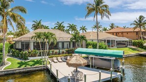 A waterfront property with a dock, lounge chairs, and a covered seating area. - Close your eyes and imagine - SW Cape waterfront home with fully Inclusive rates (Cape Coral)