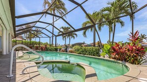 A swimming pool with a curved edge, surrounded by palm trees and tropical plants. - Close your eyes and imagine - SW Cape waterfront home with fully Inclusive rates (Cape Coral)
