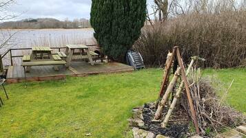 A picnic area with a wooden table and benches, a ladder, and a pile of firewood.