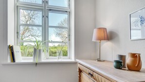 Una habitación con ventana, lámpara, planta y cómoda de madera.