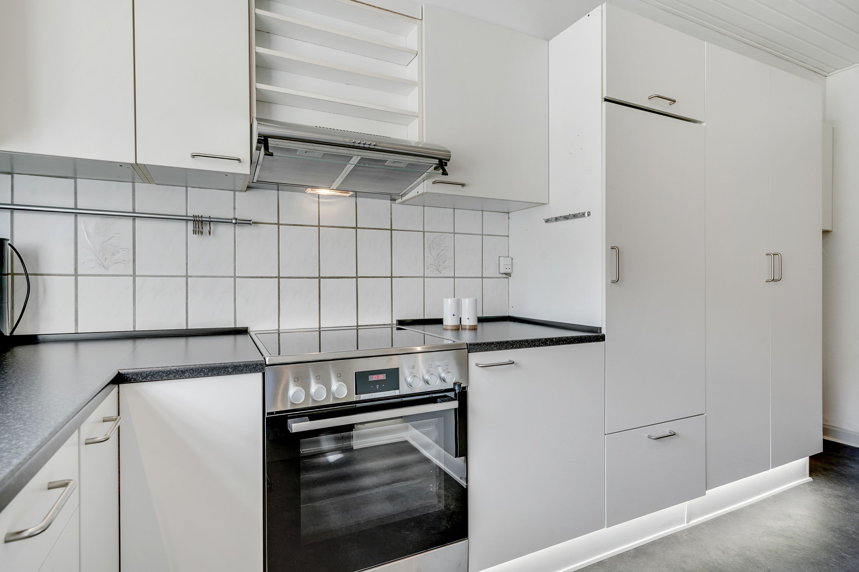 A modern kitchen with white cabinets, a stainless steel oven, and a black countertop.