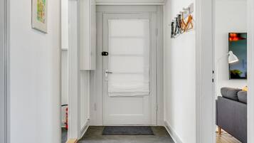 A narrow hallway with a white door, a doormat, and a gray sofa in the background.