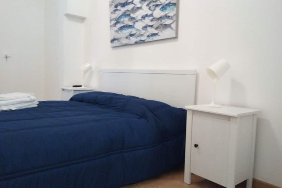 Un dormitorio con una cama, una mesita de noche, una lámpara de pared y un cuadro.