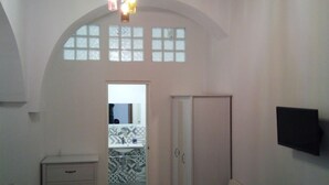 A hallway with a white wardrobe, a chair, and a TV mounted on the wall. - B&B Garibaldi (Alcamo)