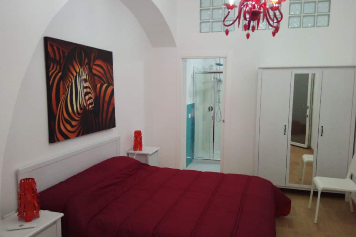 Un dormitorio con una cama grande, un armario, una ducha y una obra de arte roja en la pared.