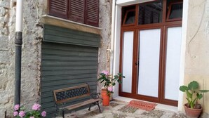 A stone building with a closed shutter, a bench, and potted plants. - B&B Garibaldi (Alcamo)