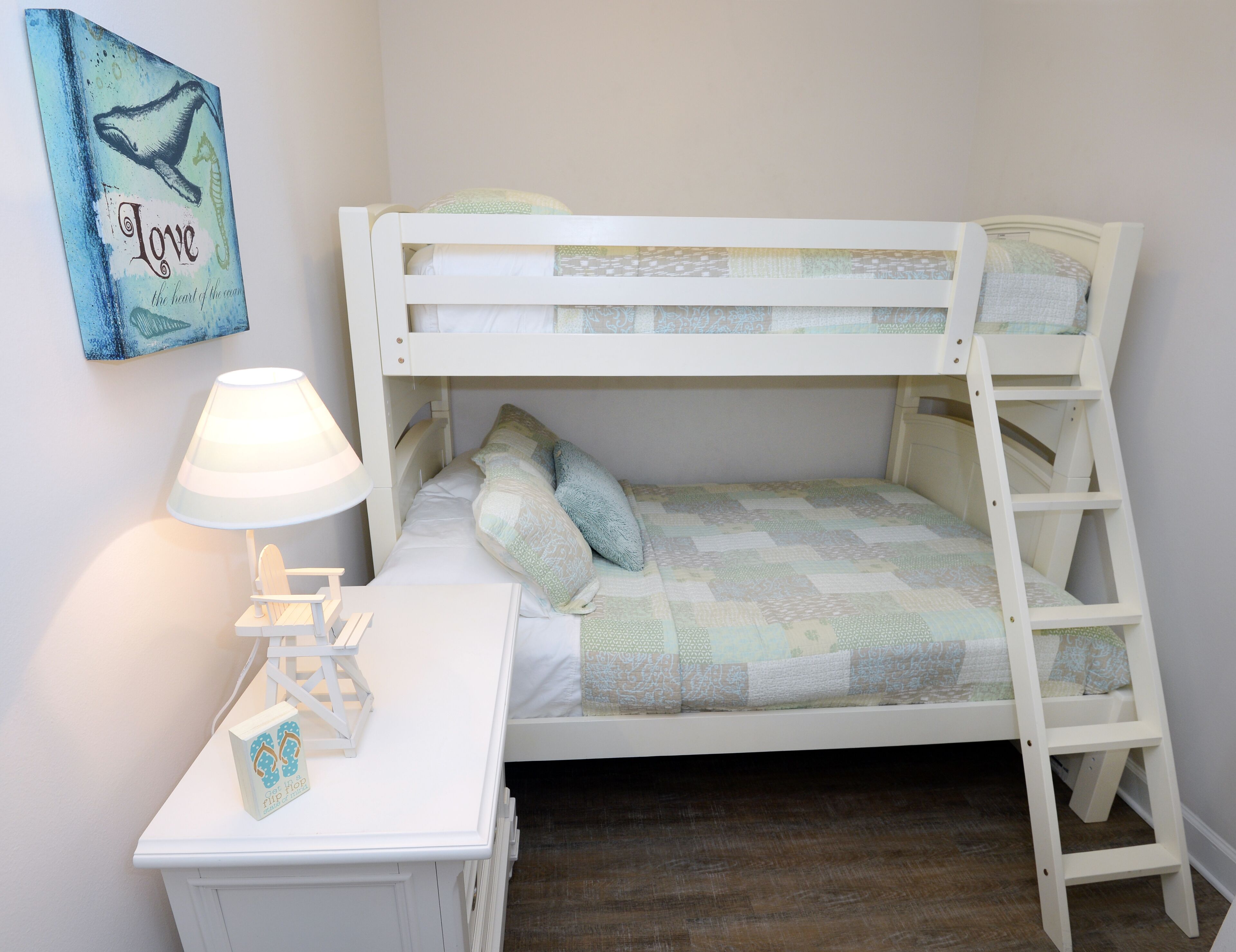 Una cama individual superpuesta con una escalera, una mesita de noche con lámpara y una decoración en la pared.