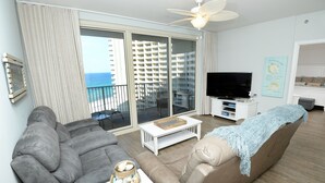 A living room with a grey sofa, a beige sofa with a blue throw, a white coffee table, and a flat-screen TV on a white stand.