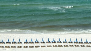 A beach with rows of sun loungers and umbrellas, a sandy shore, and the ocean in the background.